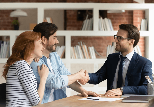 Mann schüttelt anderem Mann am Tisch die Hand, an dessen Schulter sich eine Frau lehnt, MKC Martin Kaufmann Consultation